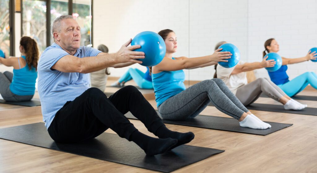 PIlates Training mit dem Ball auf der Matte, durchgeführt von jungen Menschen und vom Opa; gute Ergänzung zur ganzheitlichen Heilmassage